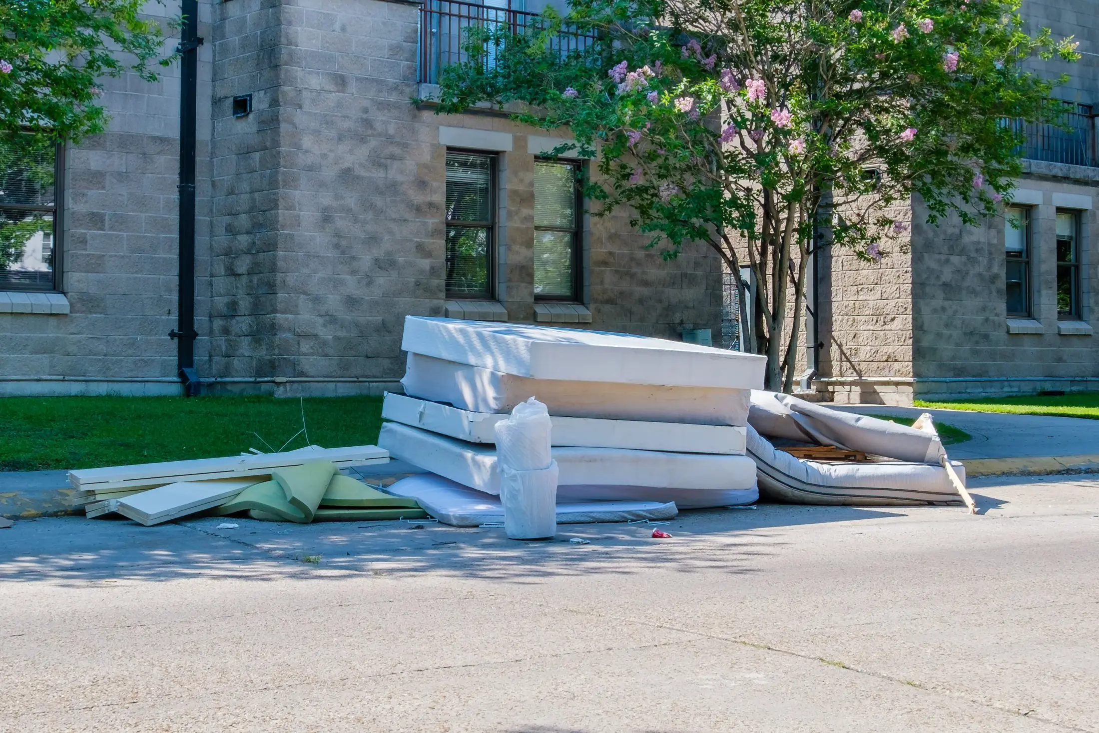 Old mattresses, a box spring and bed frame boards left at the curb on a sunny day