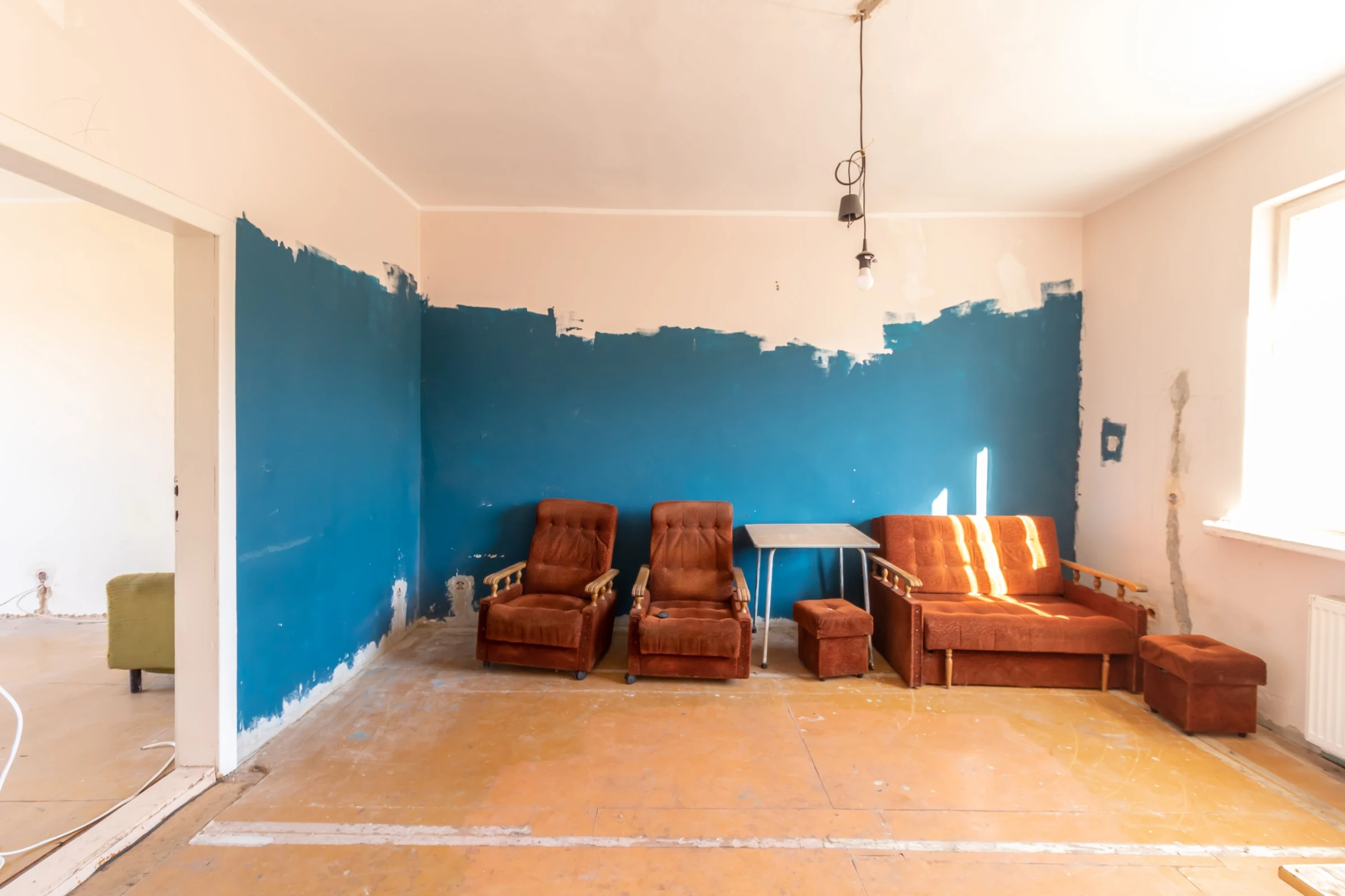 Old rust-colored armchairs and a matching sofa sitting against a freshly painted blue wall in a vacant unit