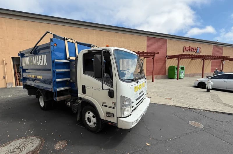 A Junk Magik junk removal truck at the curb outside a retail store on a sunny day