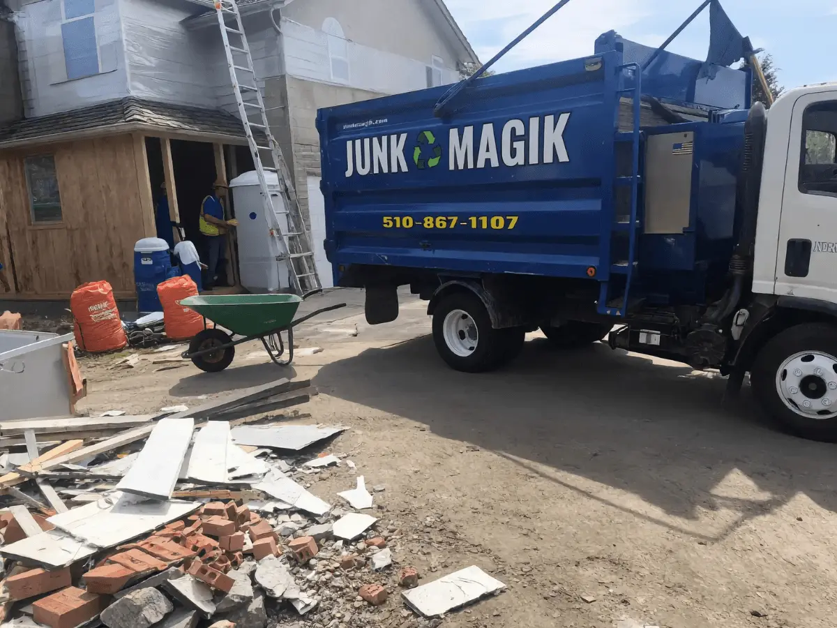 The Junk Magik truck beside broken bricks and old boards outside a home under renovation