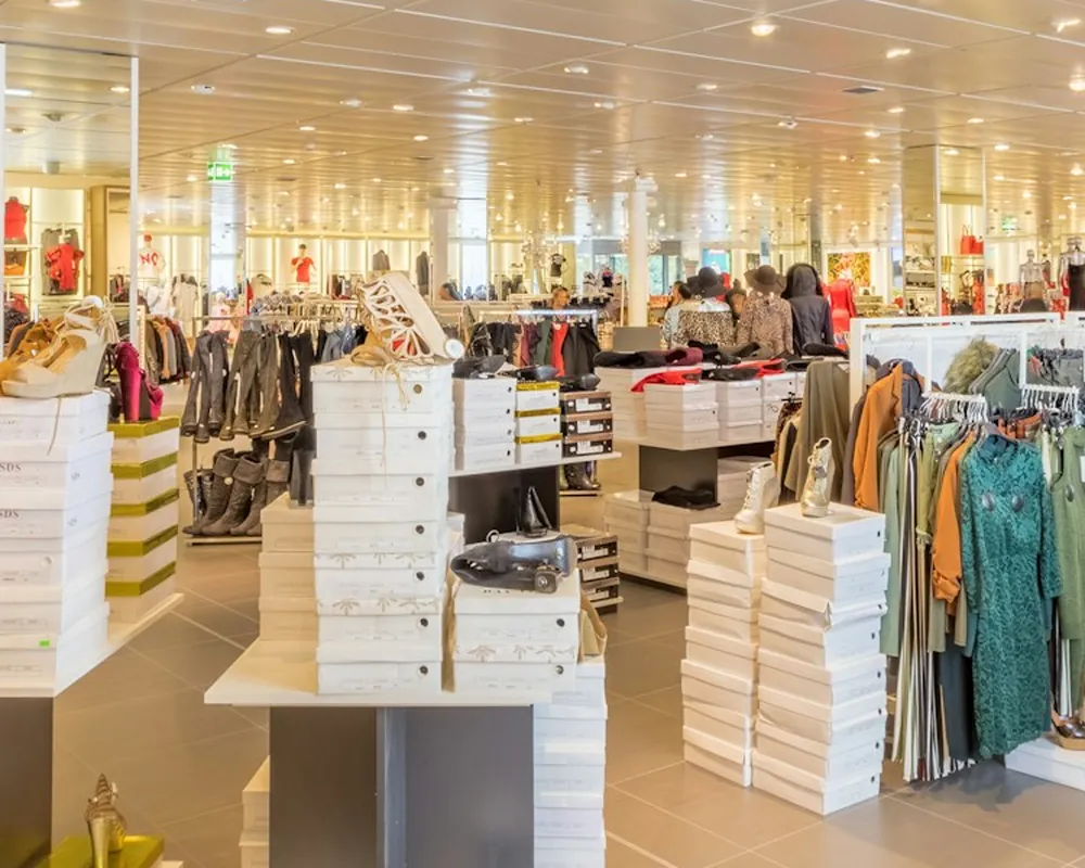 A bright clothing store floor with display tables stacked with shoe boxes and racks of clothing