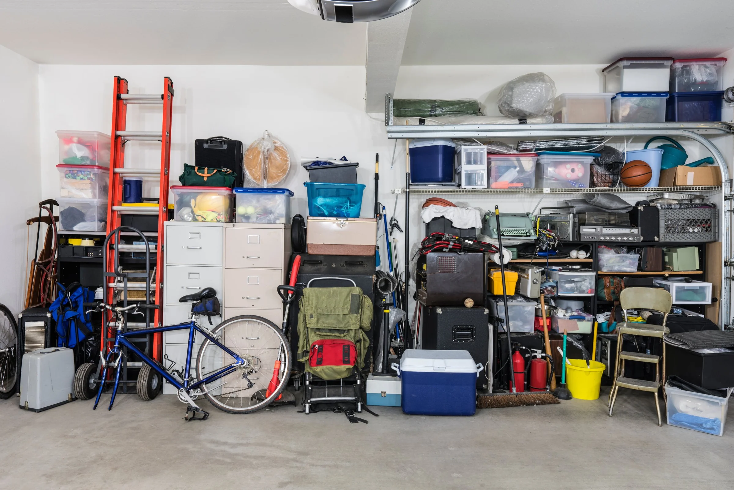 A full garage wall with storage bins stacked to the ceiling, an orange ladder, a blue bike, filing cabinets, a camping pack and a cooler